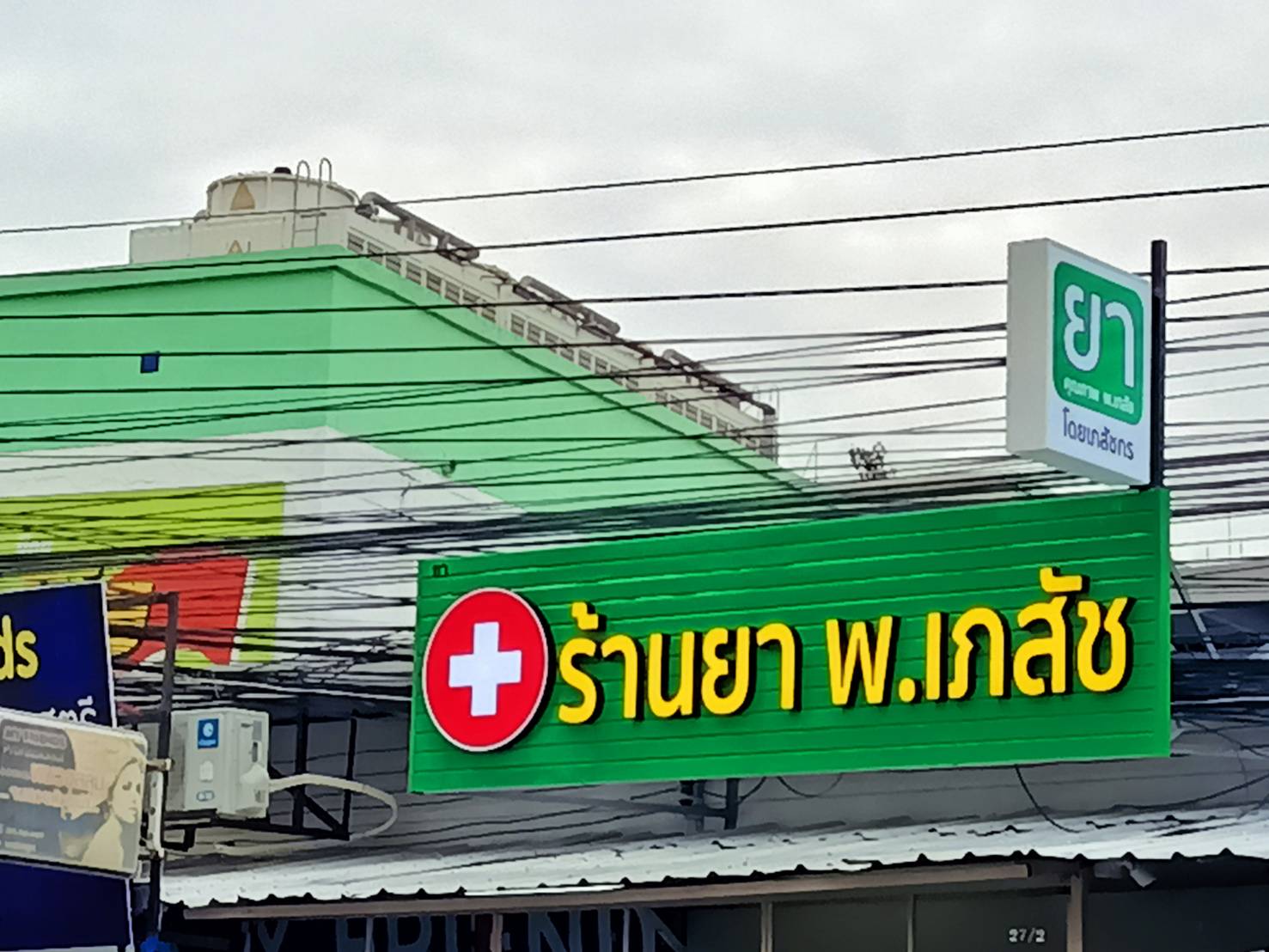 ป้ายตัวอักษรไฟออกหน้า พื้นหลังเป็นแผงตัวซีสีเขียว งานร้านยา พ.เภสัช