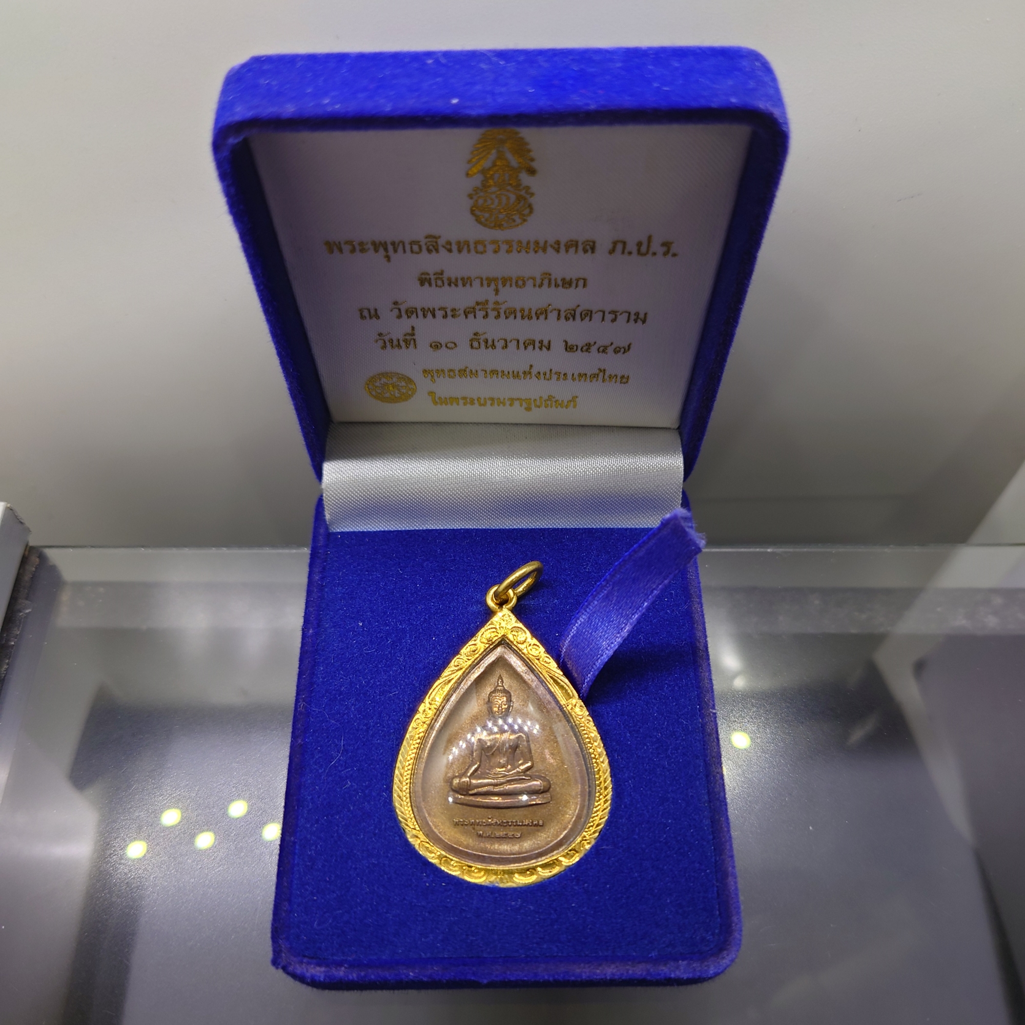 พระพุทธสิงหธรรมมงคล หลังพระปรมาภิไธย ภ.ป.ร.เนื้อนวะ พุทธสมาคมแห่งประเทศไทย ในพระบรมราชูปถัมภ์ พ.ศ.2547 เลี่ยมกรอบทองนพเก้า พร้อมตลับเดิม