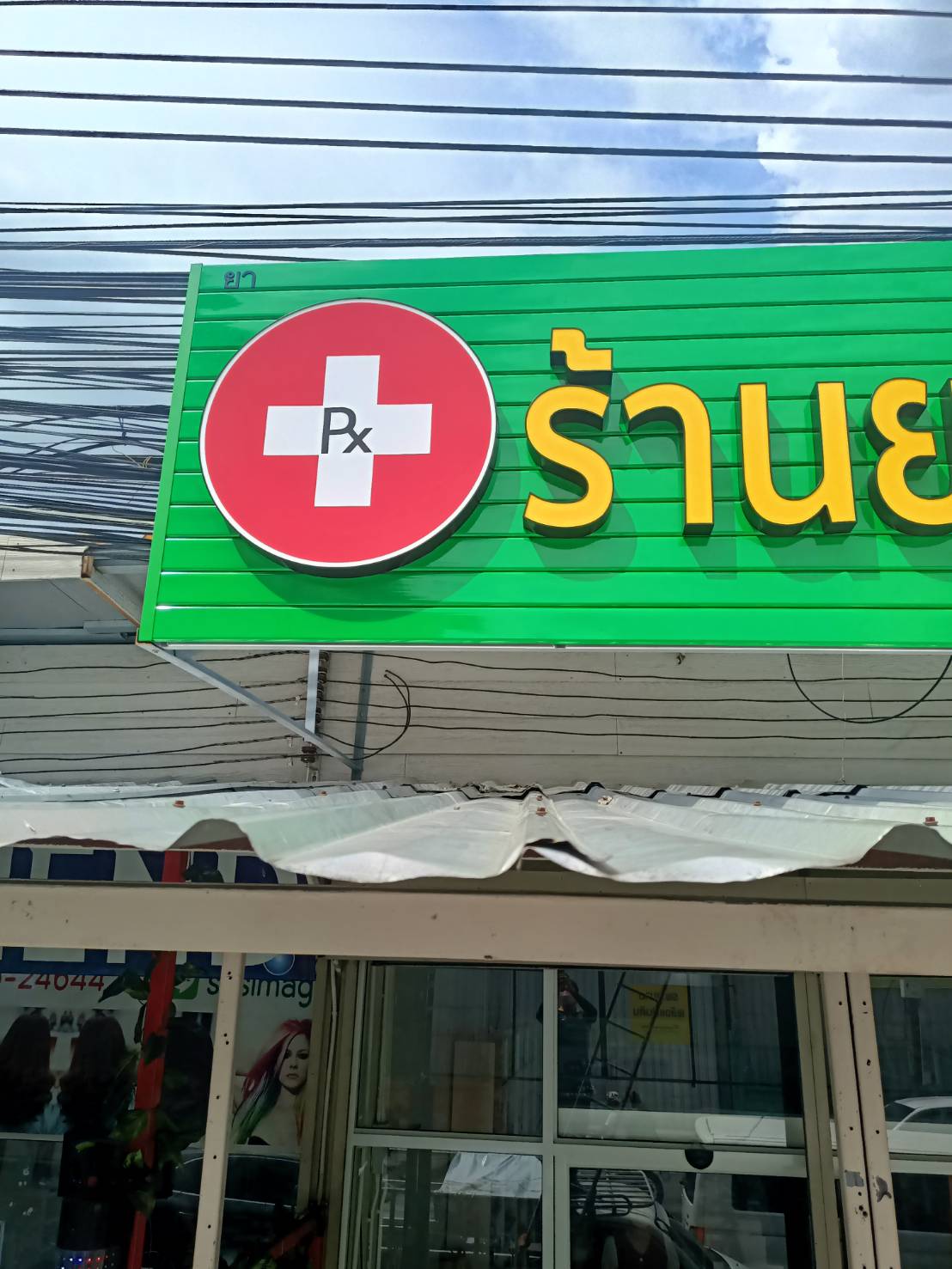 ป้ายตัวอักษรไฟออกหน้า พื้นหลังเป็นแผงตัวซีสีเขียว งานร้านยา พ.เภสัช